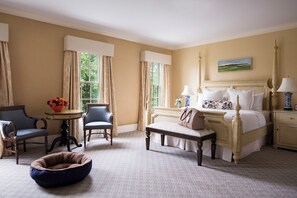 A bedroom with a bed, bedside tables, a chair, a small table with flowers, and a window with curtains. - Delamar Southport (Southport)
