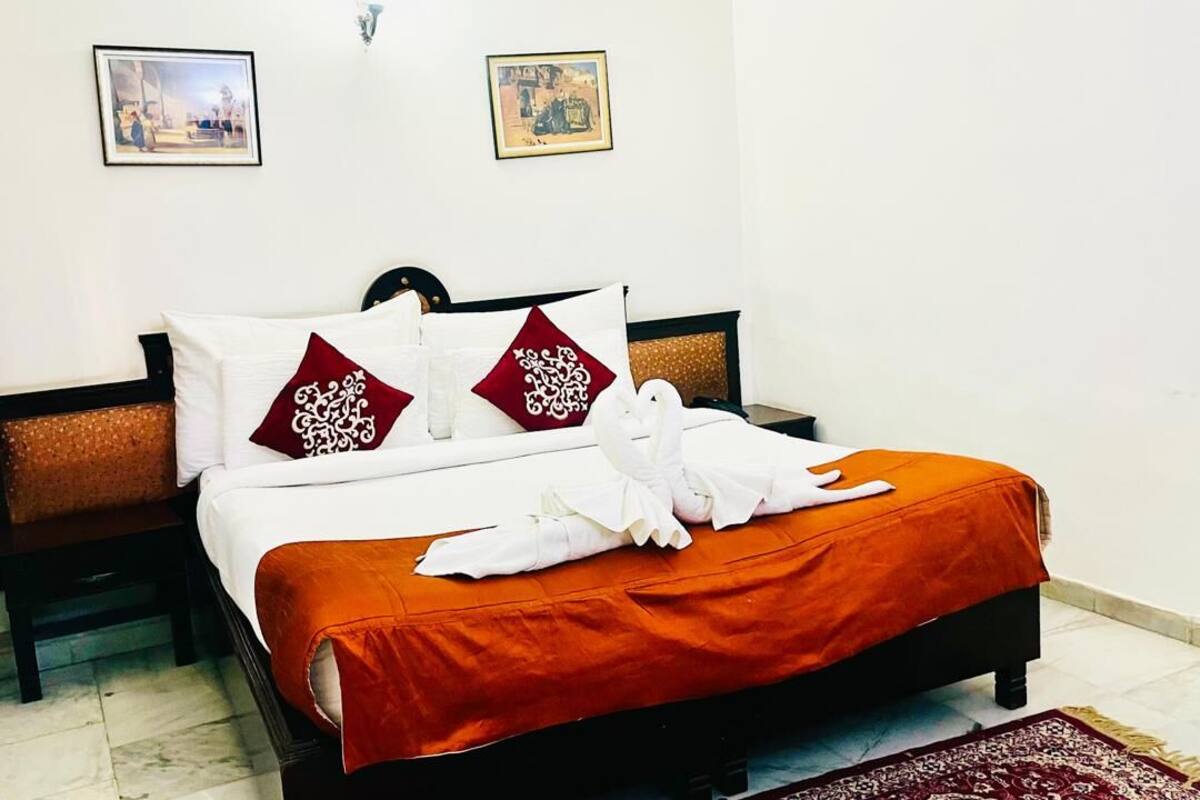 A neatly made bed with white and red pillows, a white duvet, and an orange bedspread.