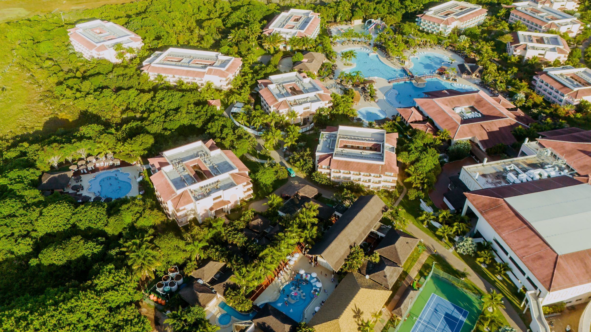 Vue aérienne d’un complexe hôtelier comprenant plusieurs bâtiments, des piscines et une végétation luxuriante.