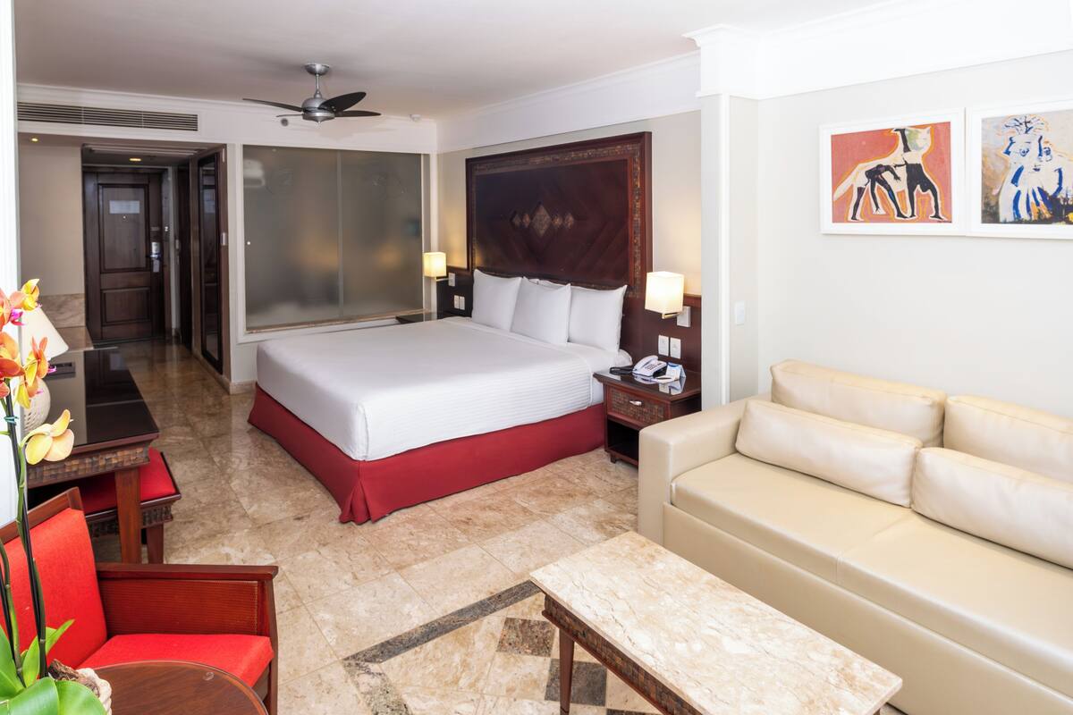 Habitación de hotel con una cama grande, un sofá, un escritorio con lámpara y cuadros en la pared.