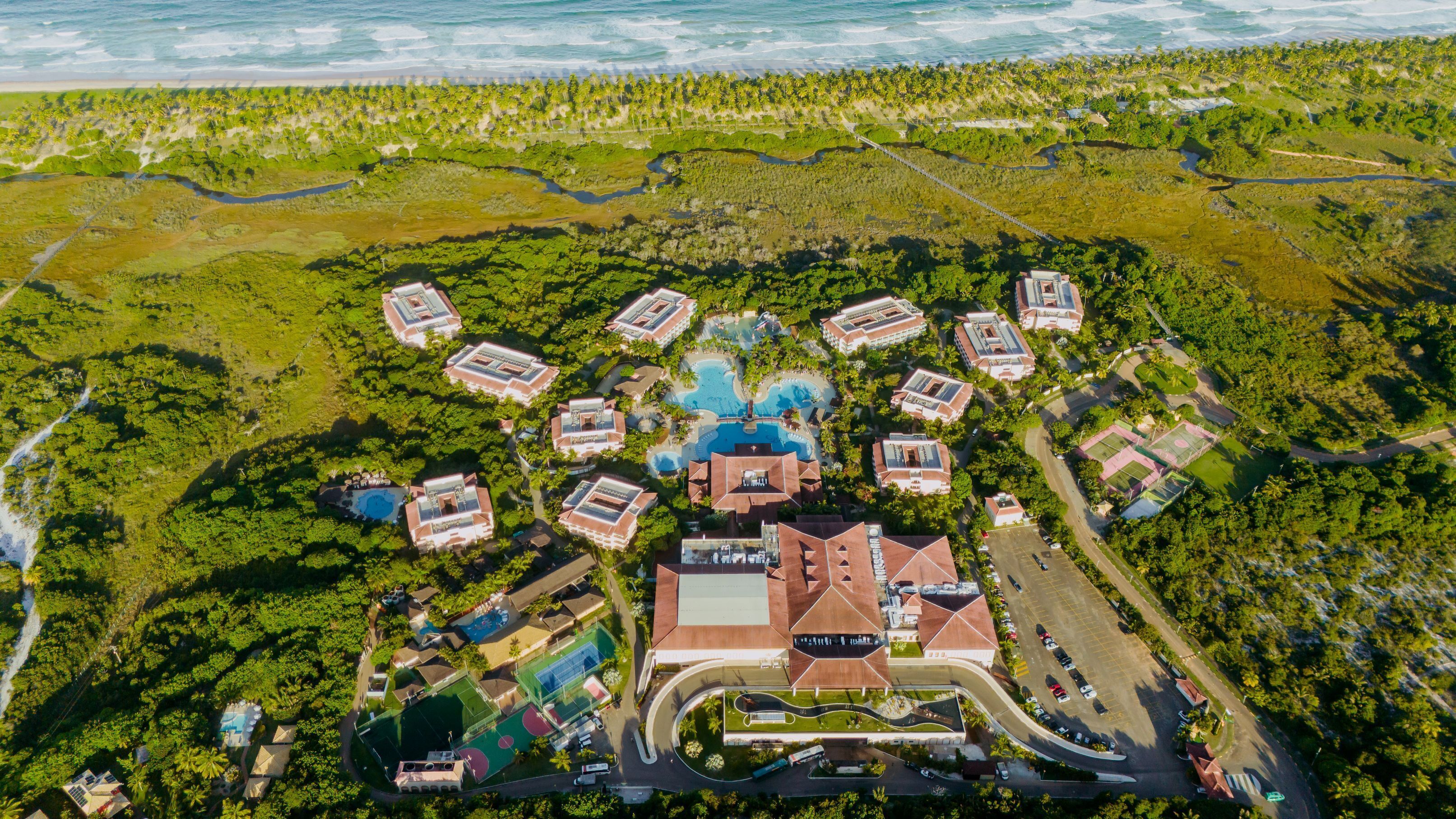 Luchtbeeld van een resort met meerdere gebouwen, een centraal gelegen zwembad en omliggend groen.