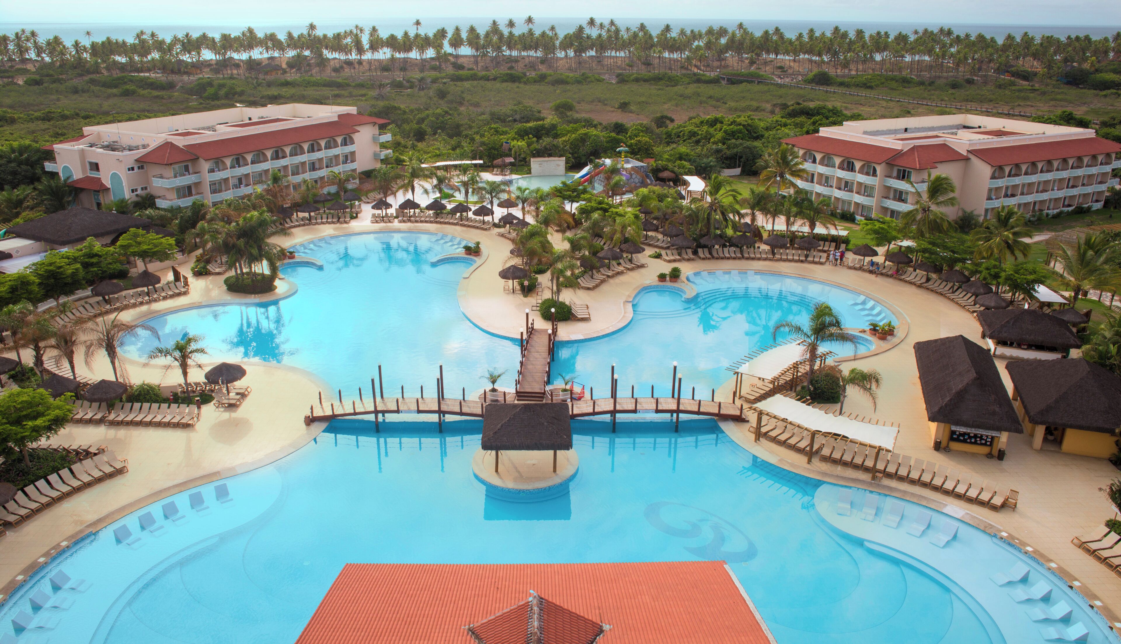 Un resort con varias piscinas, palmeras y una zona de playa.