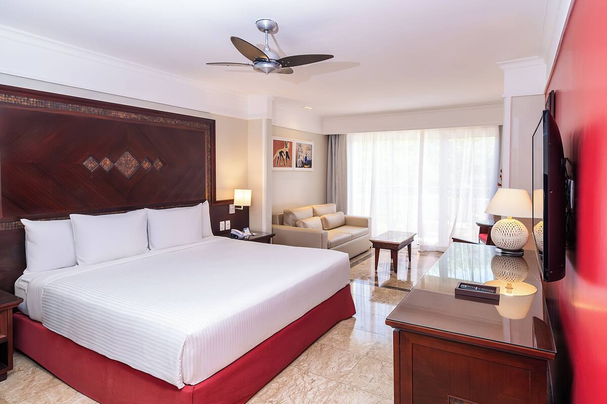 Una habitación de hotel con una cama grande, un escritorio con lámpara, un televisor y un ventilador de techo.