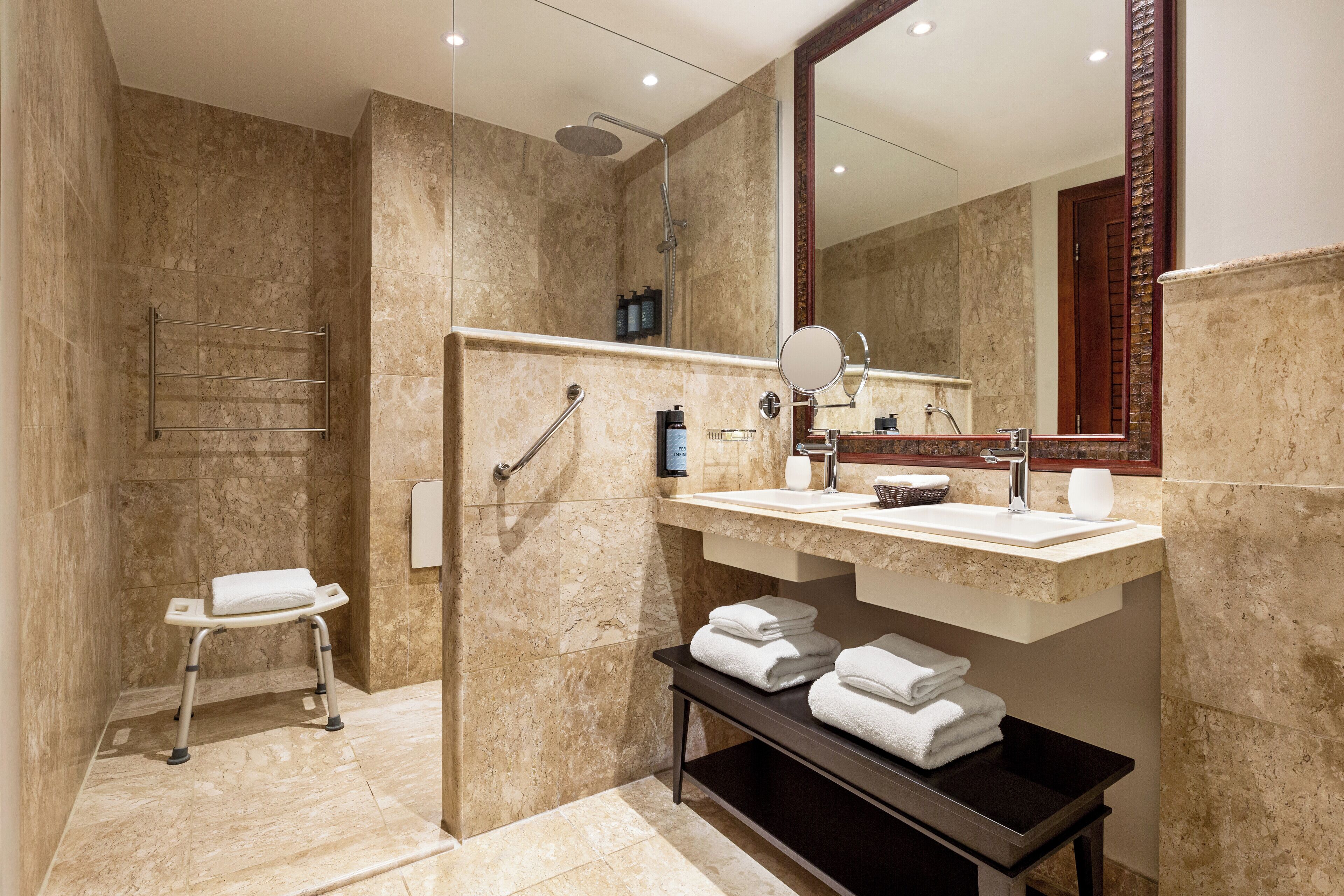 A modern bathroom with a walk-in shower, a vanity with a mirror, and a shelf with towels.