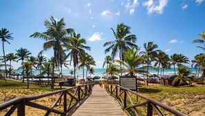 Una pasarela de madera que conduce a una playa con palmeras y sombrillas.