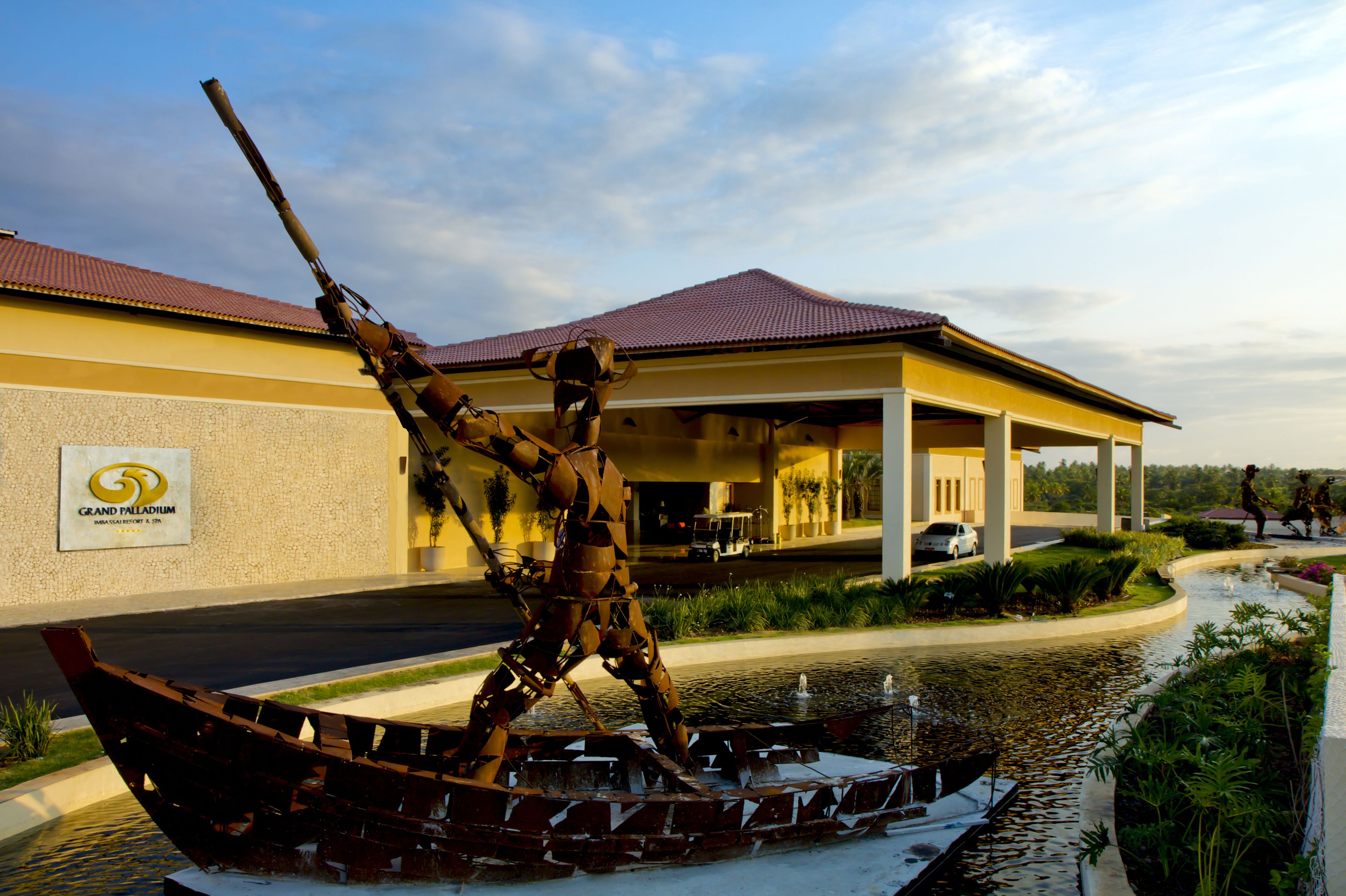 Eine Statue eines Kriegers in einem Boot vor einem Hotel mit rotem Dach und einem Schild, auf dem 'Grand Palladium' steht.