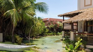 Un jardín tropical con un estanque, palmeras y una estructura de techo de paja.