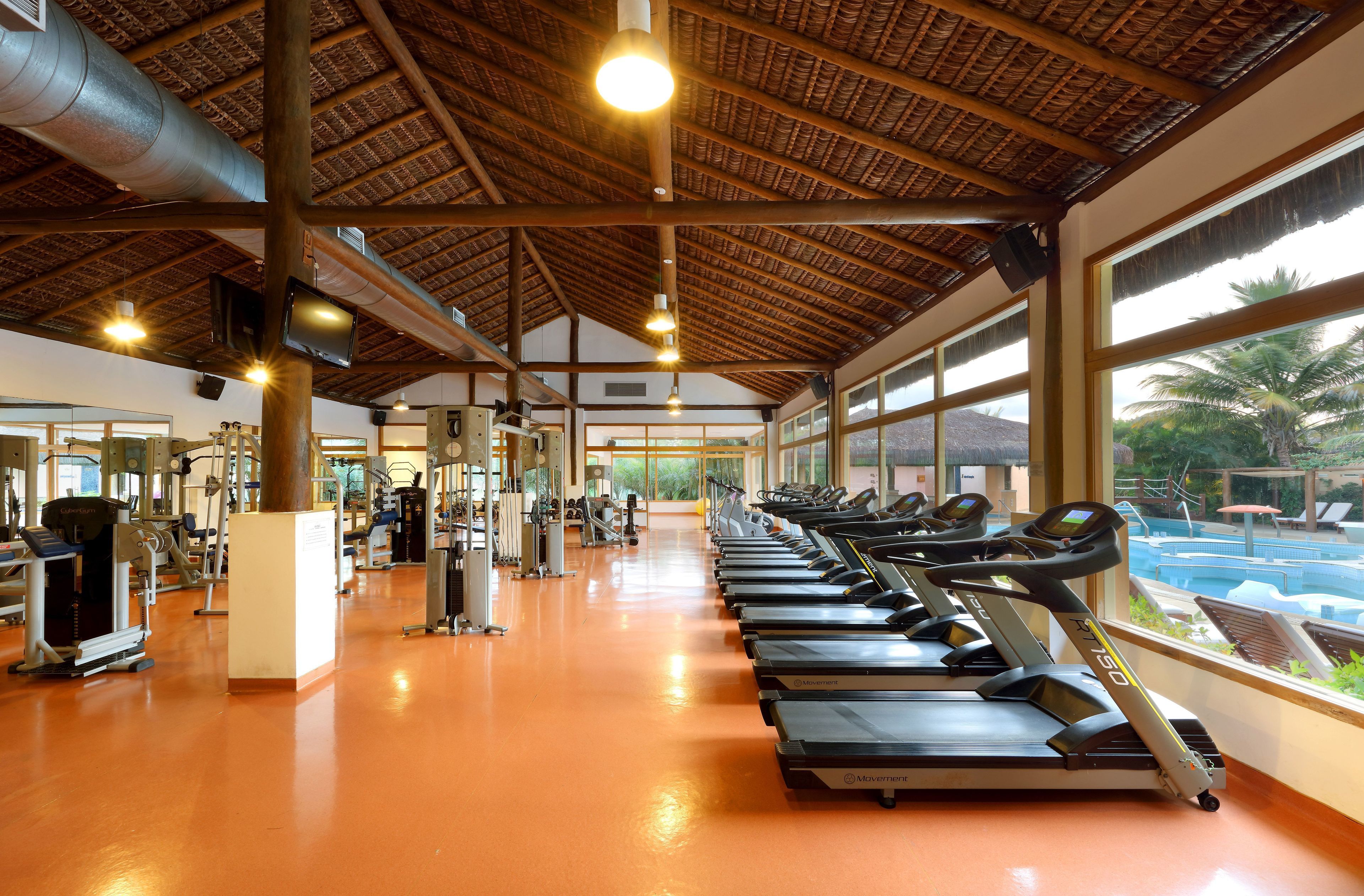 Een fitnessruimte met loopbanden, trainingsapparatuur en grote ramen met uitzicht op een zwembad.