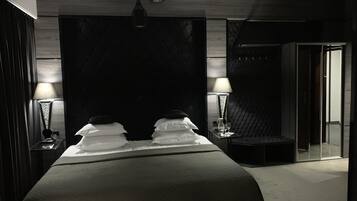 A modern hotel room with a large bed, two bedside lamps, a minibar, and a glass-enclosed shower area.