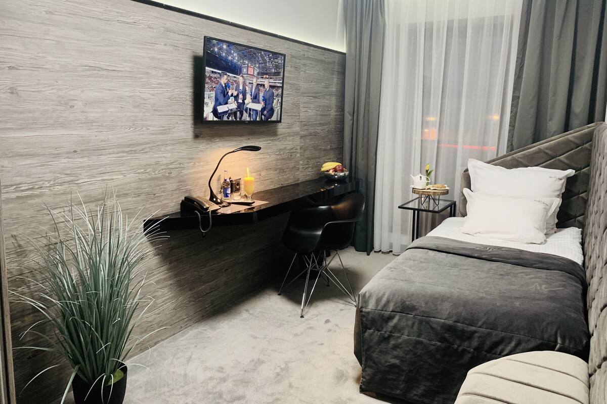 Un hotel moderno con una cama, un escritorio con una computadora, una silla, una mesita con una lámpara y un televisor montado en la pared.