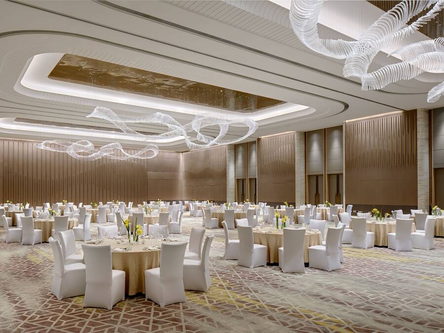 A spacious banquet hall with round tables, white chairs, and a modern ceiling design.