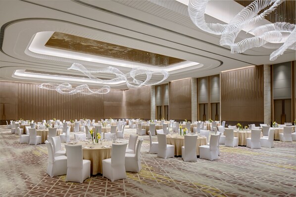 A spacious banquet hall with round tables, white chairs, and a modern ceiling design.