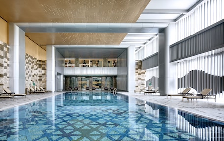 A modern indoor swimming pool with geometric tile patterns, lounge chairs, and a contemporary architectural design.