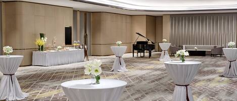 A spacious room with a grand piano, round tables with white tablecloths and flowers, and a stage with curtains.
