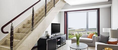 Un salon moderne avec un escalier, un téléviseur à écran plat, une table basse ronde et un canapé avec des coussins.