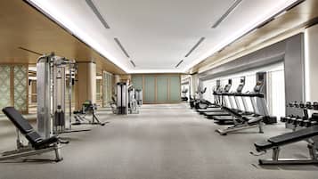 Un gimnasio con diversos equipos de ejercicio, incluyendo cintas de correr y máquinas de pesas, dispuesto en un espacio amplio.