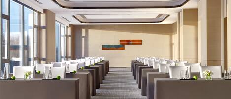 A conference room with rows of white chairs, a carpeted floor, and large windows on one side.