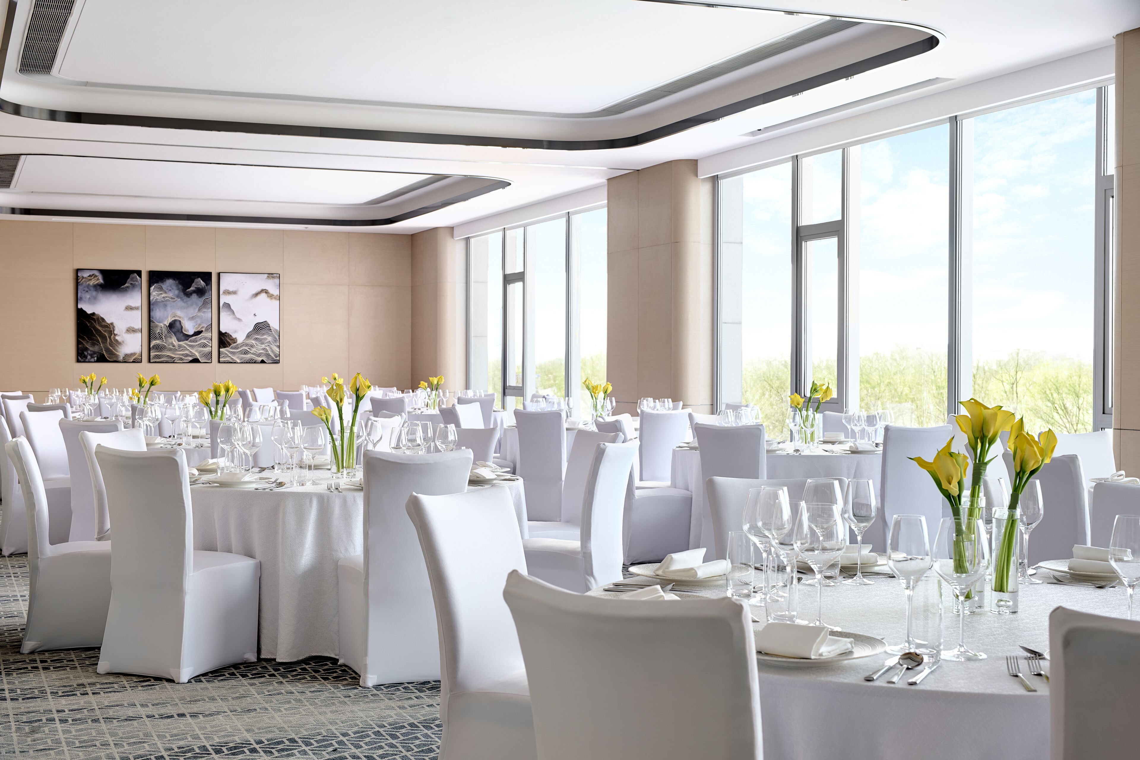 Uma sala de banquetes com mesas redondas, cadeiras brancas e centros de mesa florais.