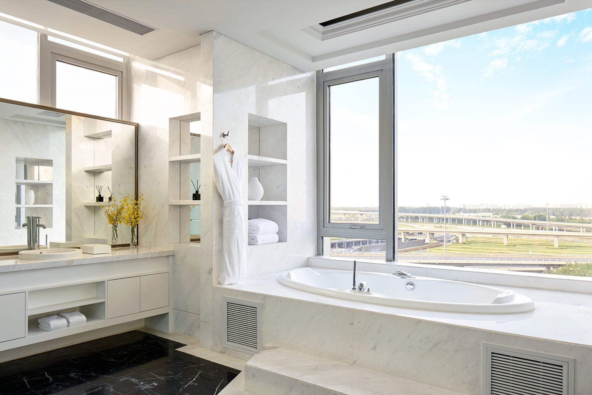 A modern bathroom with a large window, a bathtub, and a vanity with a mirror.
