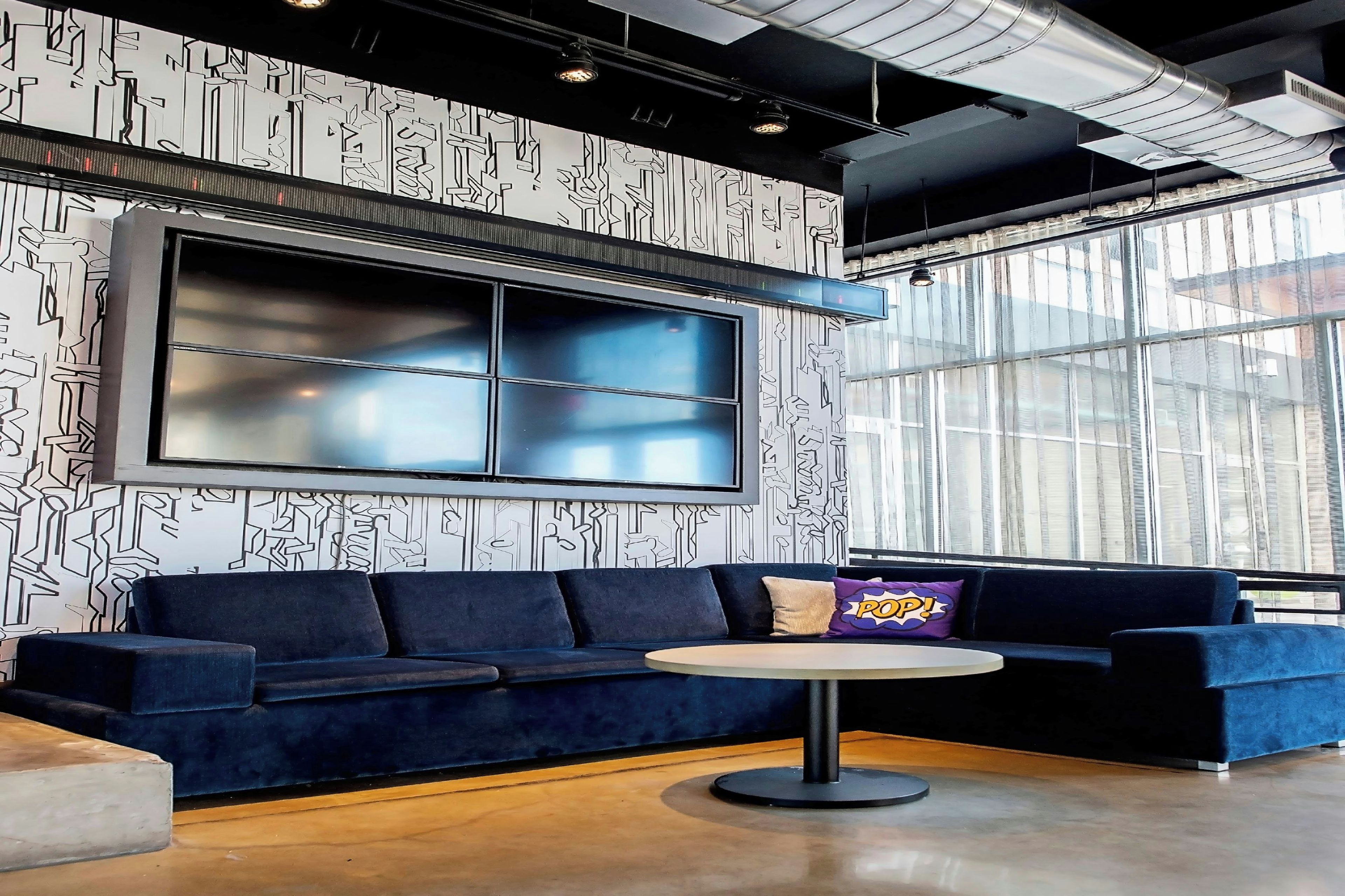 A modern lounge area with a dark blue sofa, a round table, and a large wall-mounted TV.