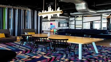A modern lounge area with a wooden table, black chairs, and a colorful geometric rug.