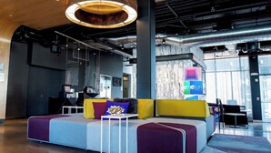 A modern lobby with a sectional sofa, a hanging light fixture, and a view of the outside. - Aloft by Marriott Tulsa (Tulsa)