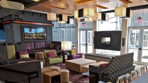 A modern lounge area with a sofa, chairs, a coffee table, and a flat-screen TV. - Aloft by Marriott Tulsa (Tulsa)