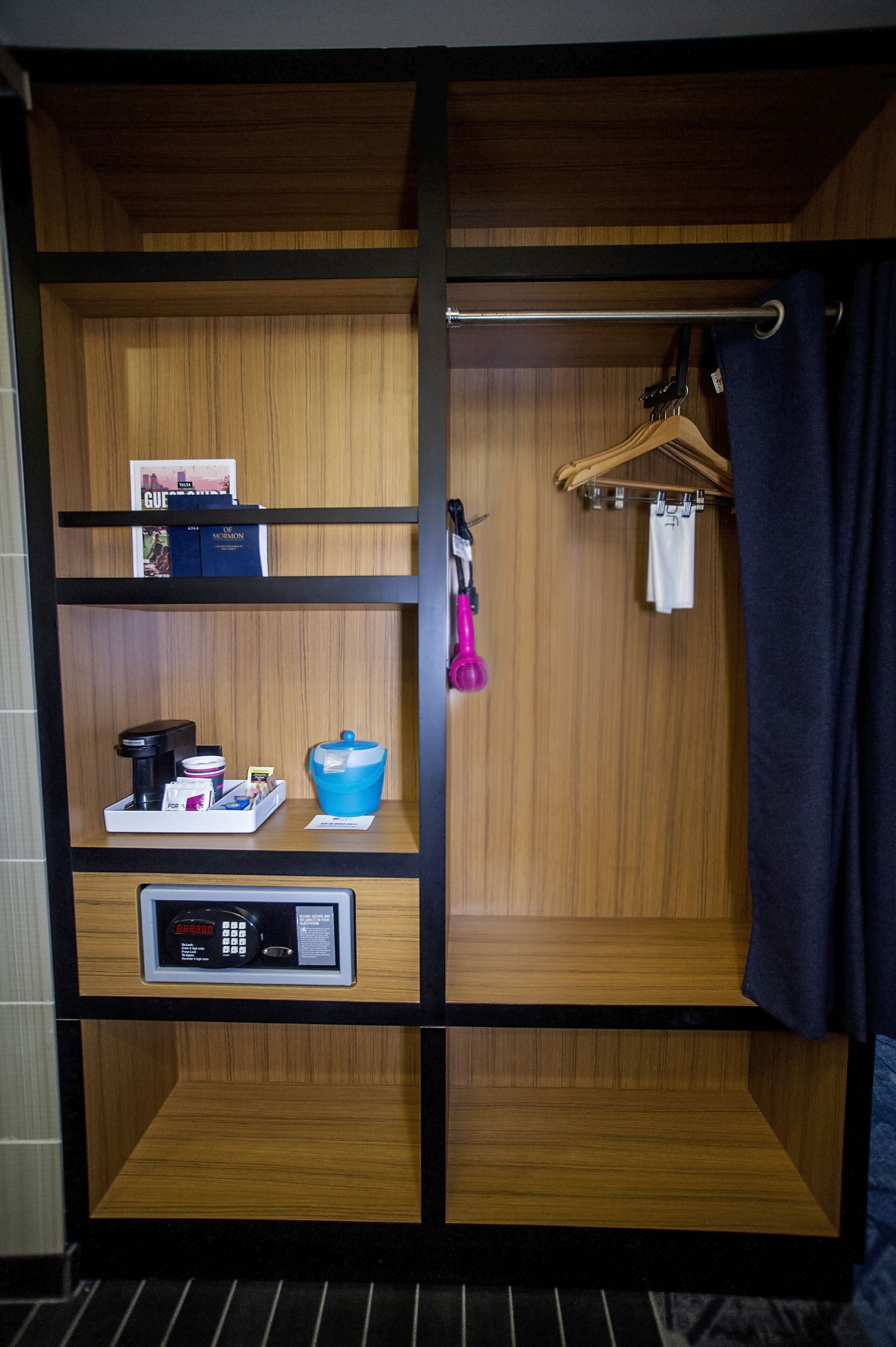 A hotel room with a wooden wardrobe, a small shelf with toiletries, a hanging shower curtain, and a towel rack.