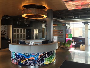 A modern reception area with a graffiti-style wall, a circular counter, and a digital clock displaying the time. - Aloft by Marriott Tulsa (Tulsa)