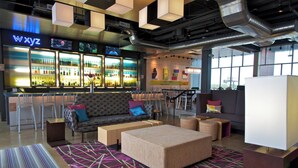 A modern bar area with a neon sign, seating arrangements, and a large window providing a view. - Aloft by Marriott Tulsa (Tulsa)
