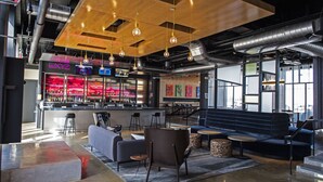 A modern bar area with a bar counter, seating, and hanging light fixtures. - Aloft by Marriott Tulsa (Tulsa)