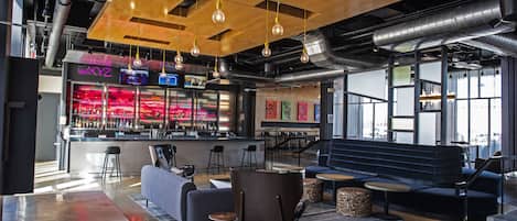 Un área de bar moderna con mostrador, asientos y lámparas colgantes.