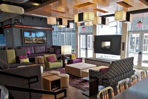 A modern lounge area with a sofa, chairs, a small table, and a TV screen. - Aloft by Marriott Tulsa (Tulsa)