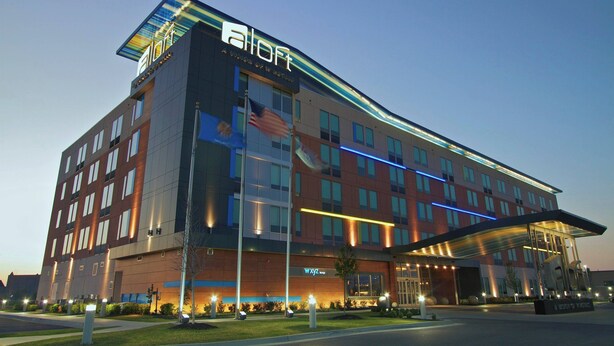 A modern hotel with a prominent 'All-In-One' sign, multiple floors, and a covered entrance area. - Aloft by Marriott Tulsa (Tulsa)
