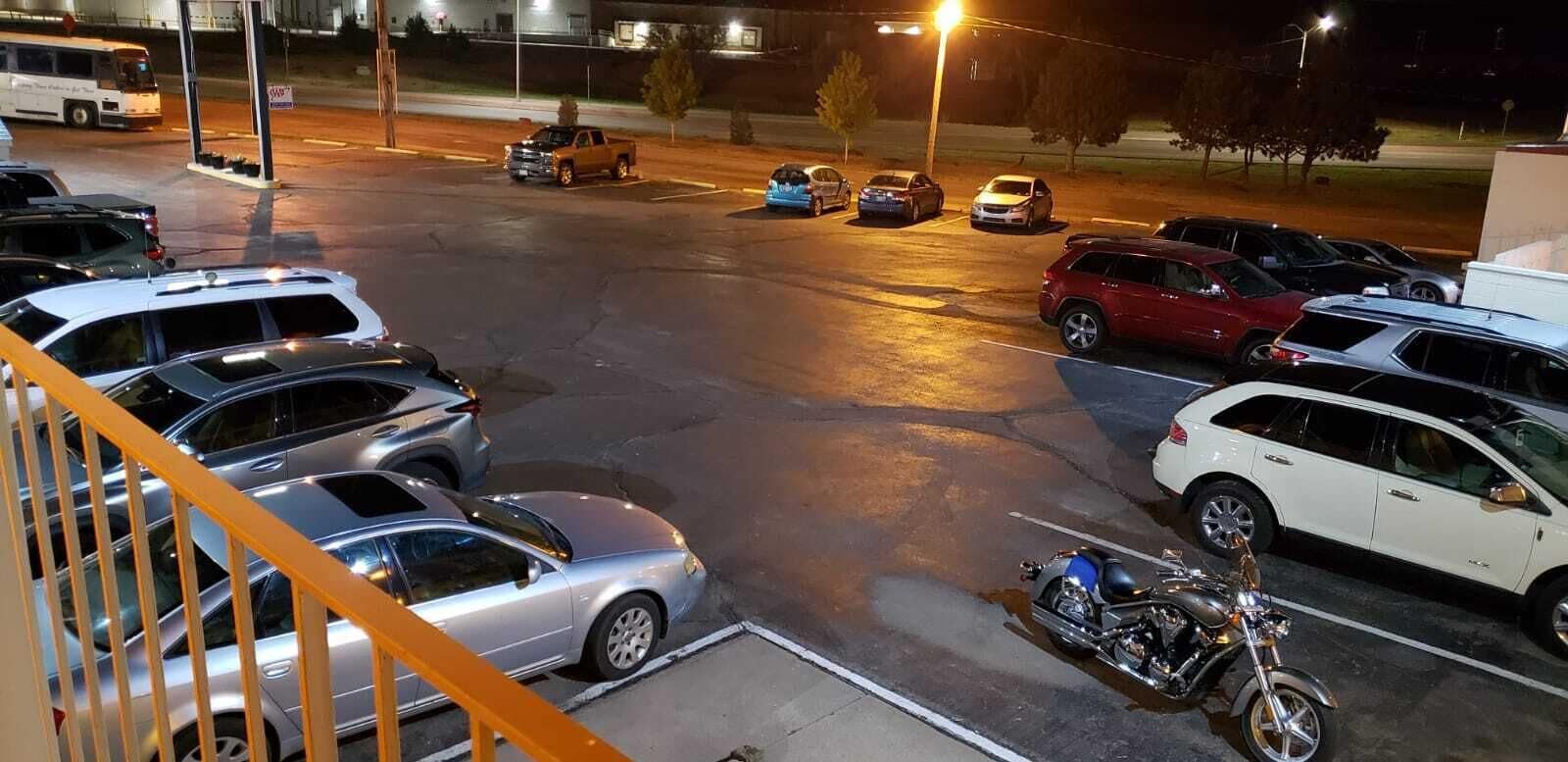 A parking lot with several cars and a motorcycle, a bus in the background, and a building with a sign that reads "W".