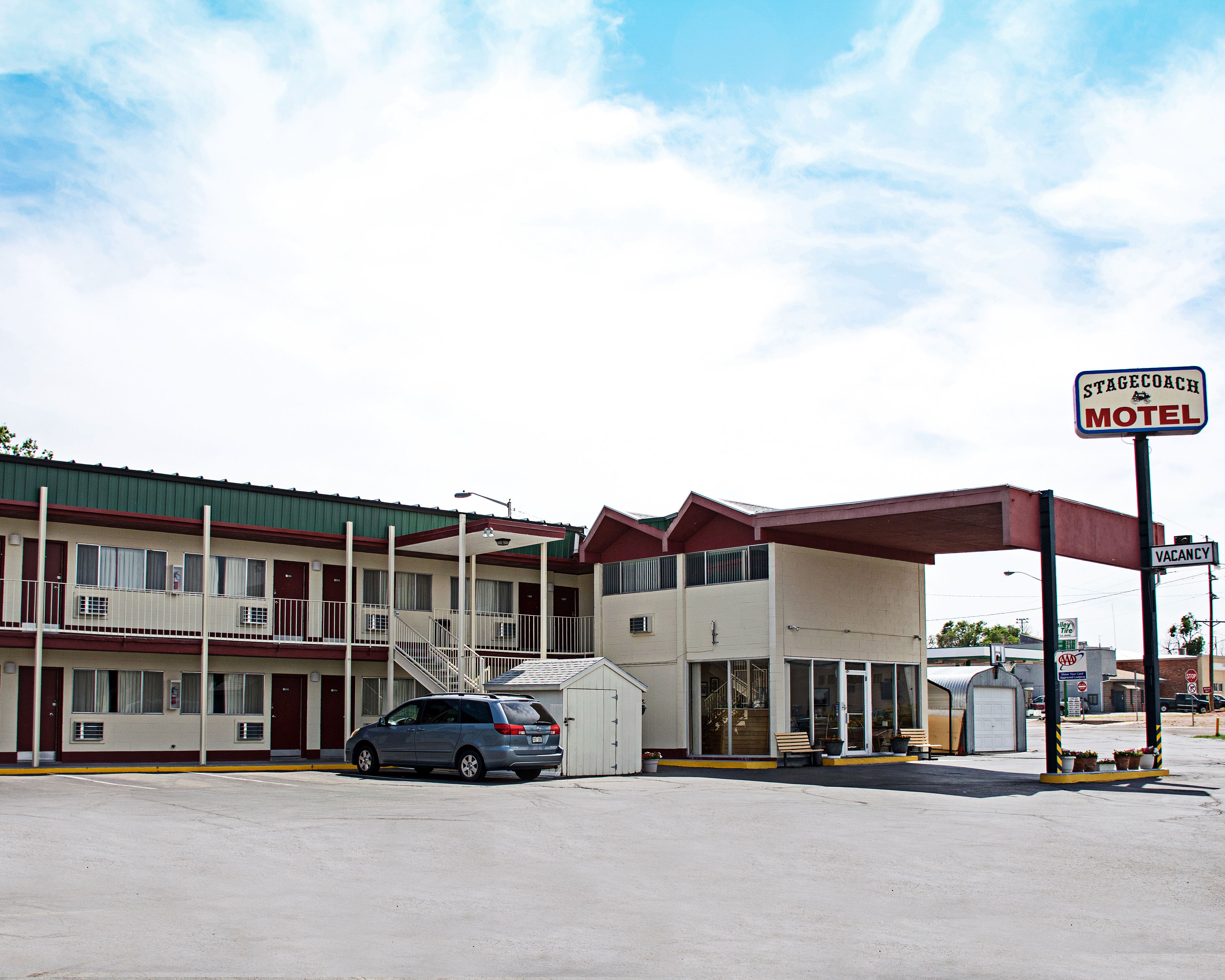 Um motel com área de estacionamento coberta, um carro estacionado na frente e uma placa indicando quarto disponível.