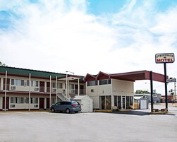 Un motel con área de estacionamiento techada, un coche estacionado al frente y un letrero que indica disponibilidad.