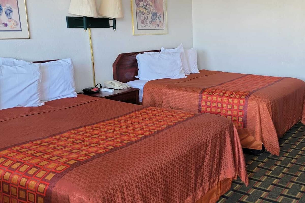 Une chambre d’hôtel avec deux lits, un bureau, une chaise, un téléphone et une télévision.