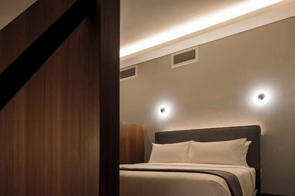 A modern hotel room with a bed, wooden paneling, and recessed ceiling lights.