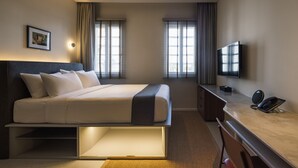 Een moderne hotelkamer met een bed, bureau, televisie en een schilderij aan de muur.