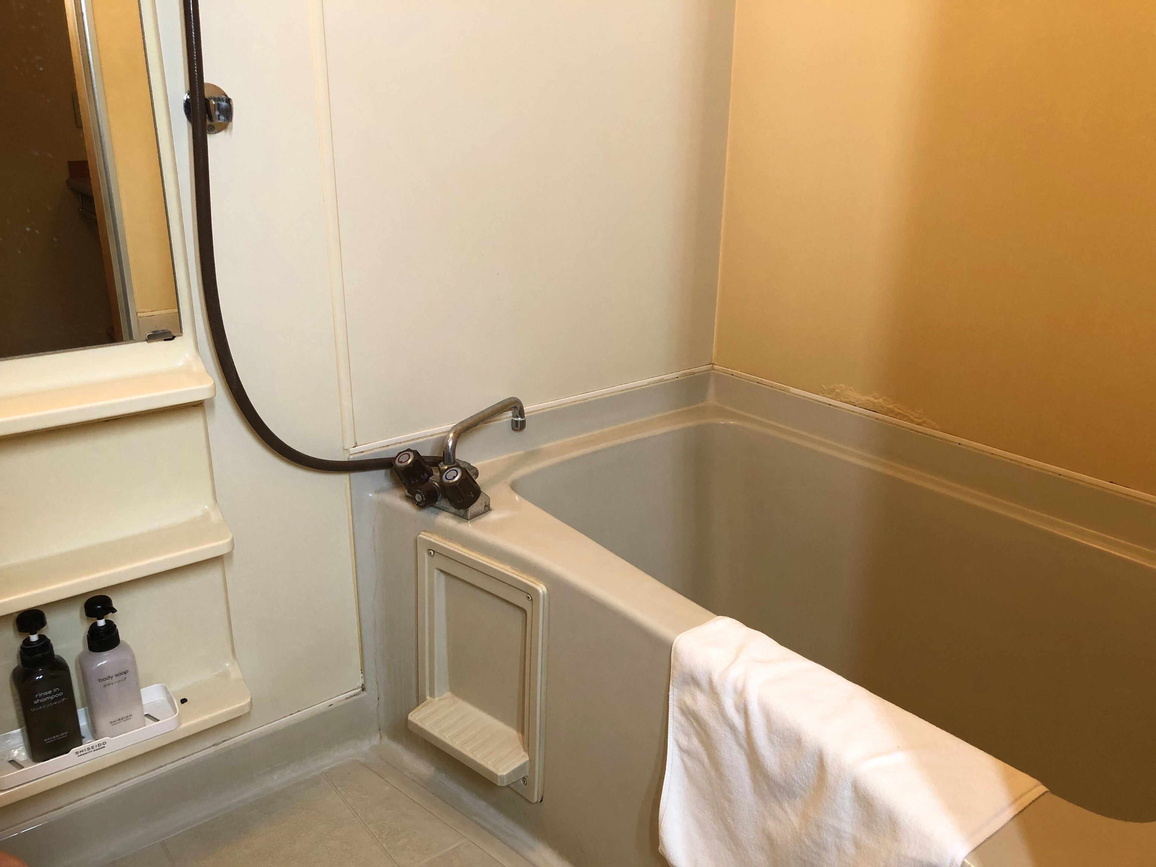A bathroom with a bathtub, a window, and a shelf with toiletries.