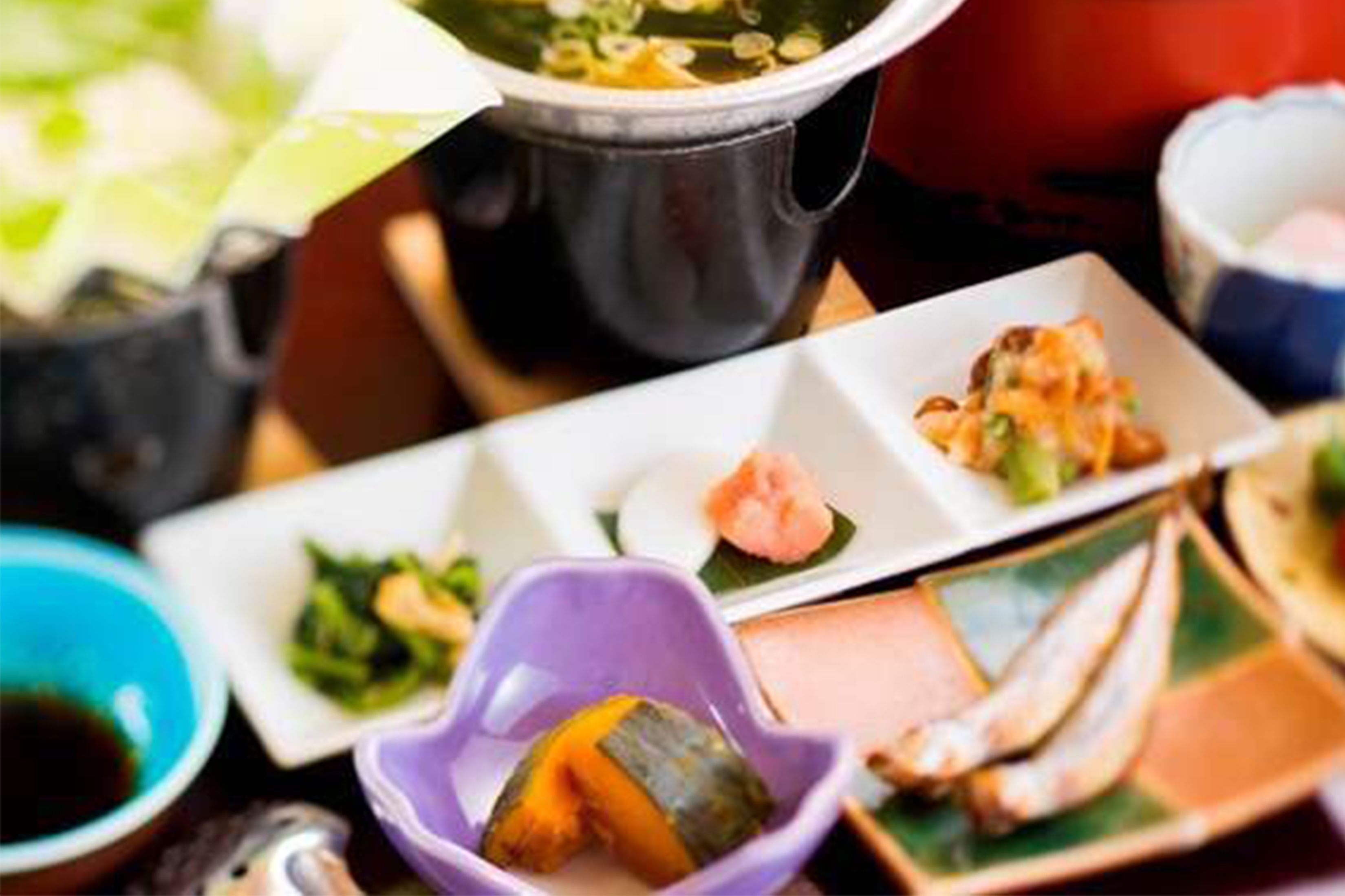 A variety of dishes on a table, including a bowl of soup, a plate with a rolled item, and several small dishes with different food items.