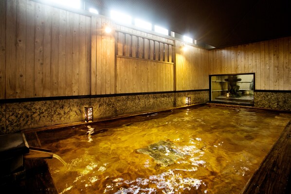 Un interior de madera con un baño de aguas termales, paredes de madera y suelo de piedra.