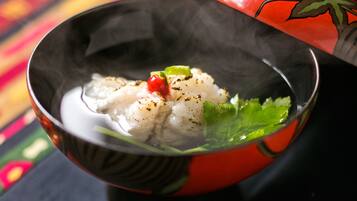 A bowl of white food with green leaves and a red garnish, placed on a table with a colorful patterned cloth.