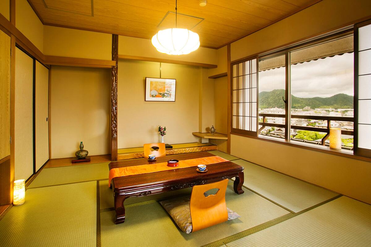 A traditional Japanese room with tatami flooring, a low wooden table, and a view of a mountainous landscape through a shoji screen.