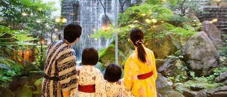 A family of four in traditional attire observing a waterfall in a lush garden setting.