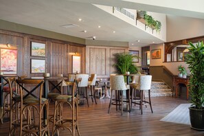 A spacious interior with wooden flooring, a mezzanine level, and various seating arrangements including bar stools and chairs. - The Coed-Y-Mwstwr Hotel (Bridgend)