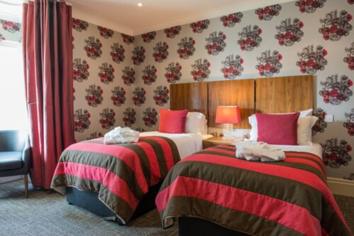 A hotel room with two beds, a wooden headboard, a nightstand, a lamp, and a chair.