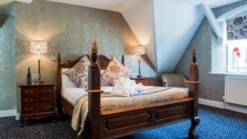 A bedroom with a large bed, two bedside tables, a nightstand, patterned wallpaper, and a window with a view.