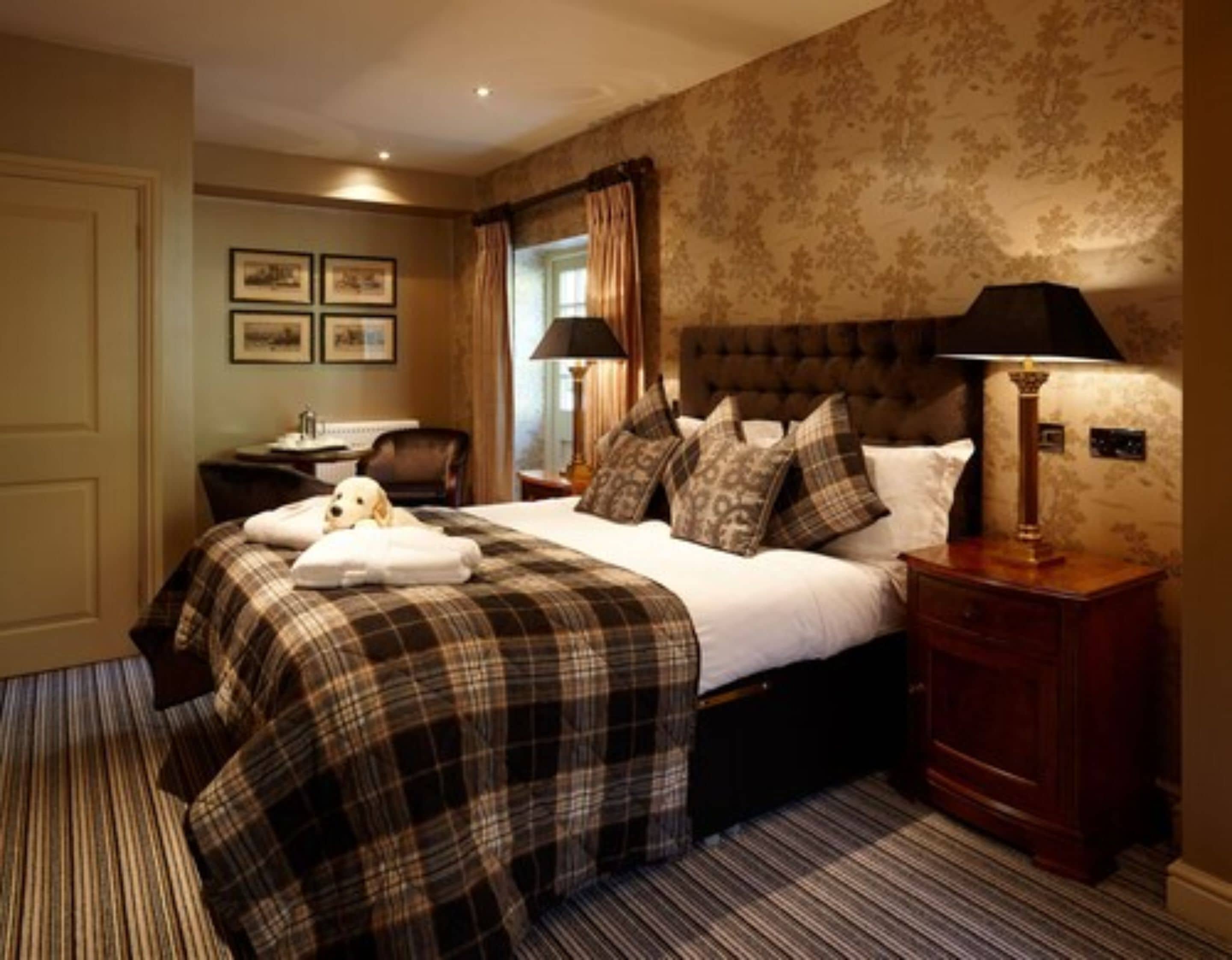 Une chambre d’hôtel avec un grand lit, un bureau et une chaise. Les murs sont ornés de tableaux encadrés et il y a une fenêtre avec des rideaux.